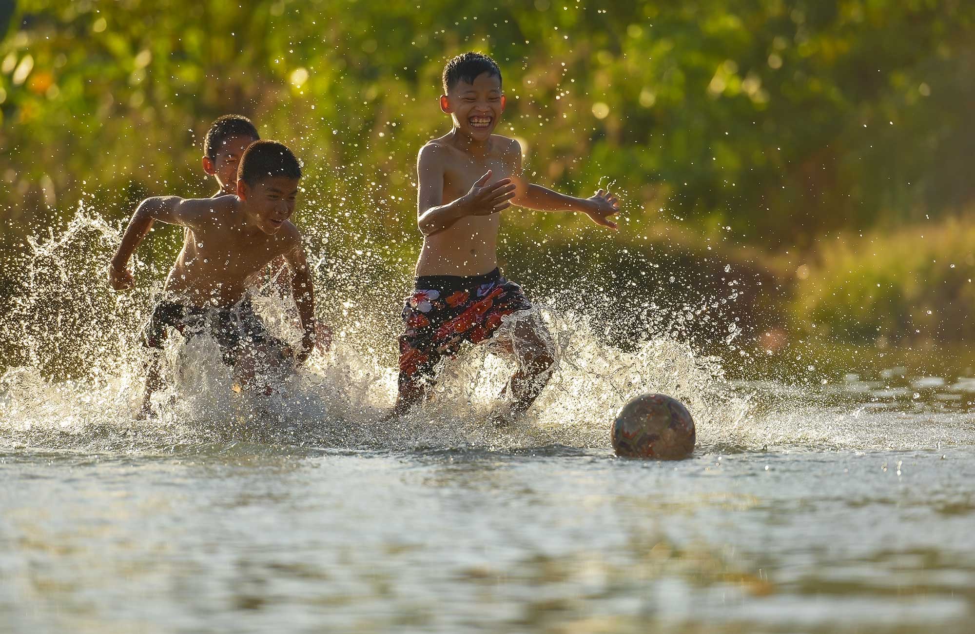 volunteering-asia-cambodja-three-boys-playing-african-football-in-water-cover