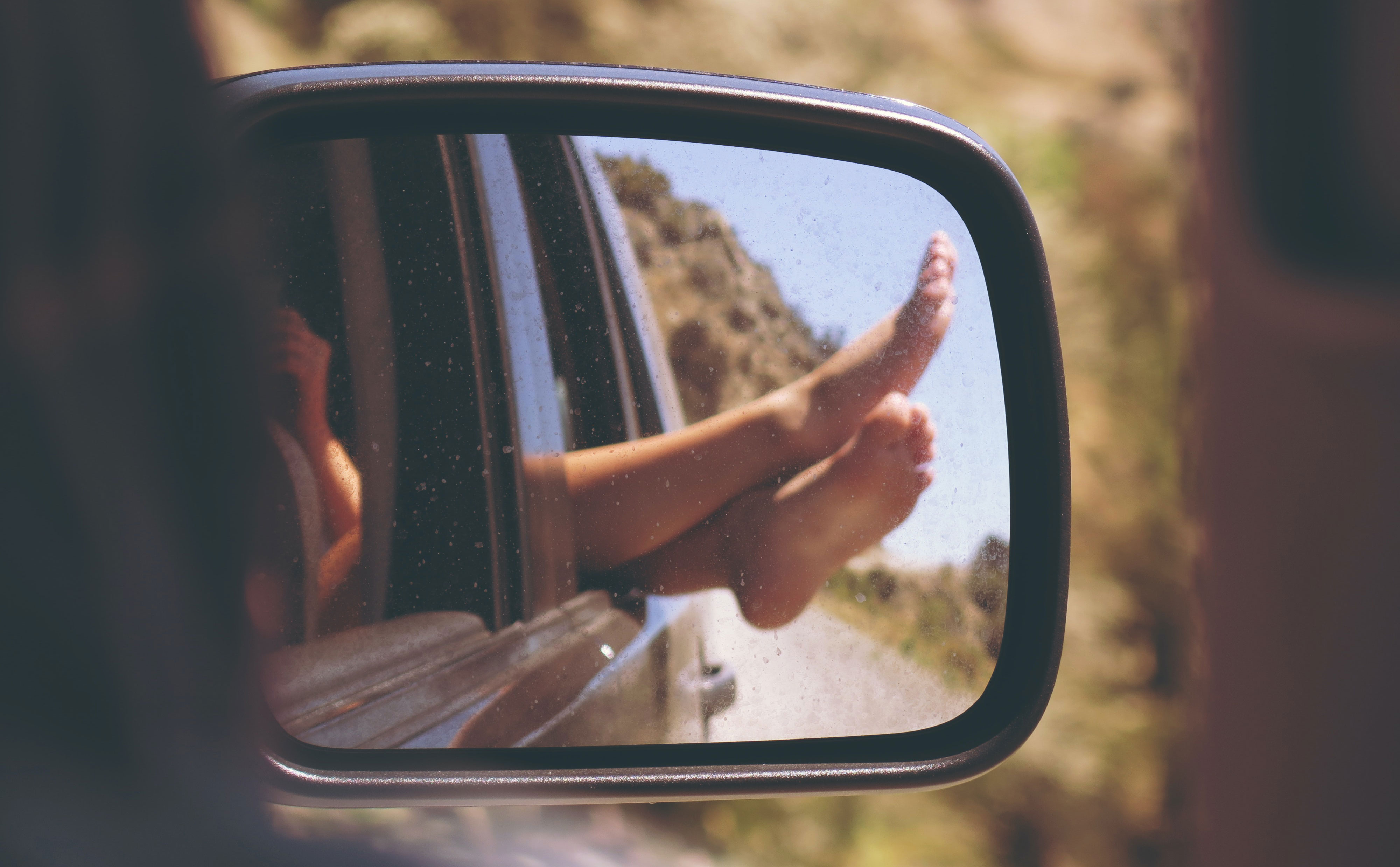 Pair of feet sticking out a car window as seen from a rear view mirror
