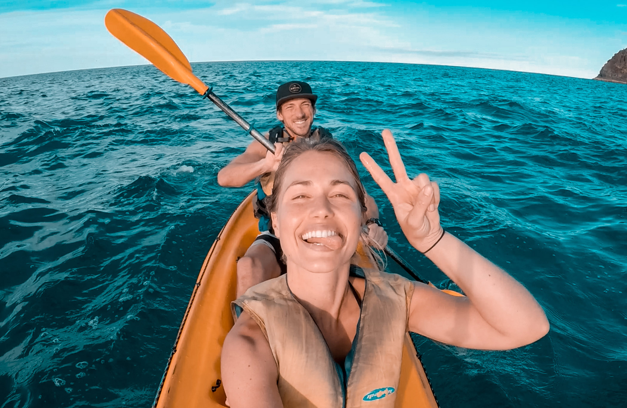 Girl and a boy smiling in the camera while kayaking in an orange kayak off the coast of Australia
