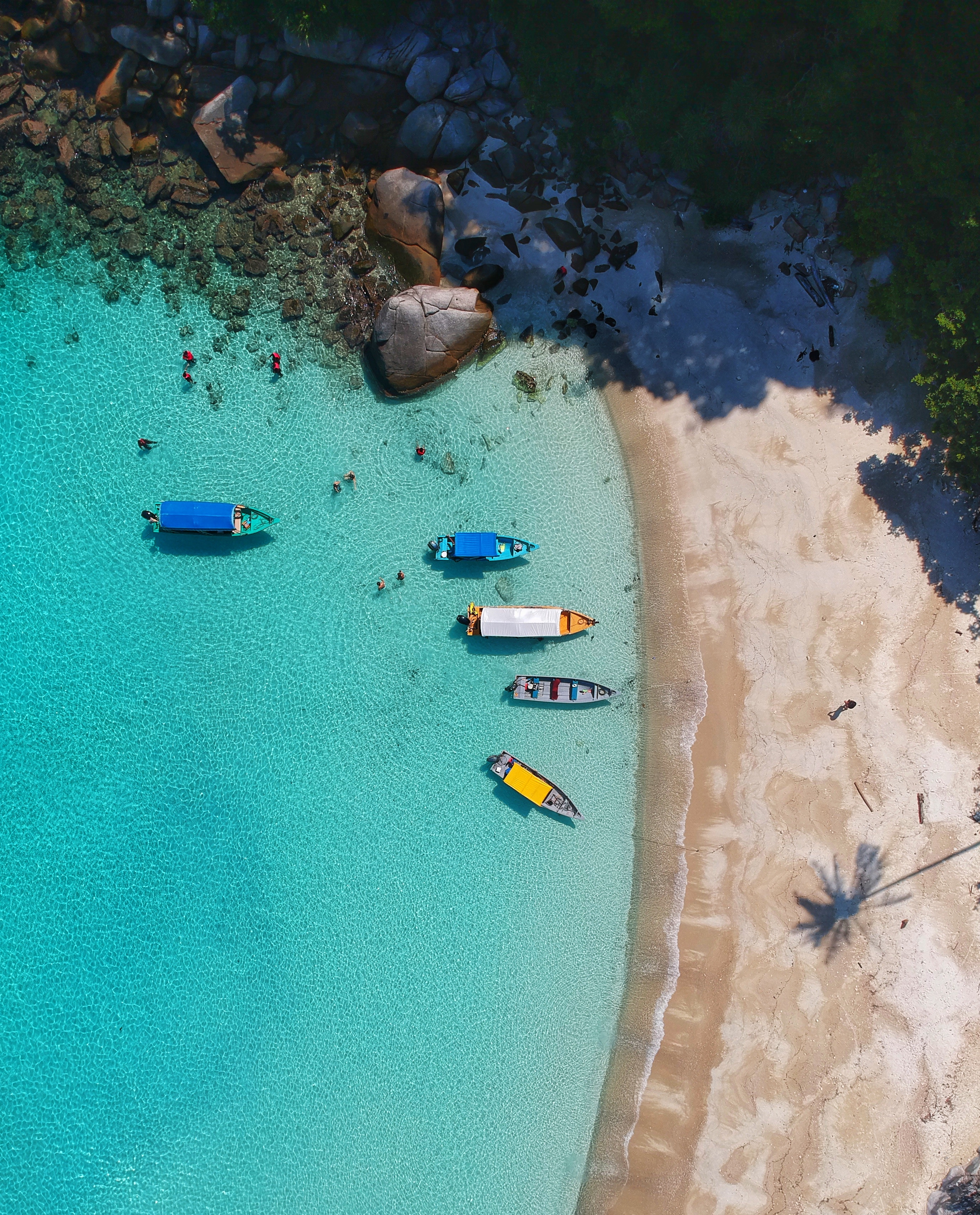 top down view of an empty sandy beach, with crystal clear water and small boats in the ocean