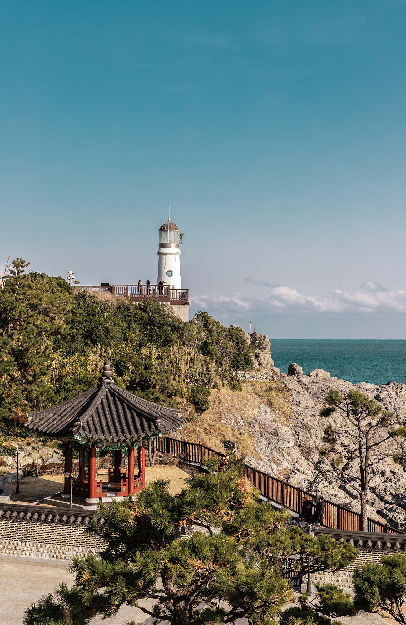 Lighthouse on a cliff in Busan, against a clear blue sky and calm ocean