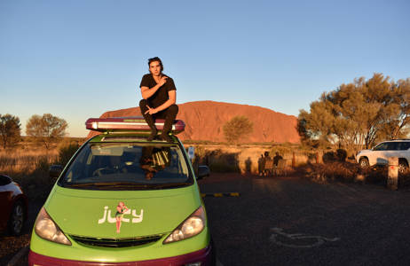 oliver on top of a jucy van in front of Uluru in Australia