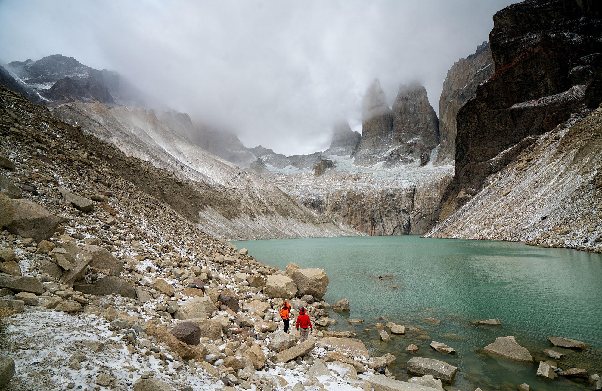 Two hikers at a lake in Tierra del Fuego National Park, with the mountain tops covered by fog.