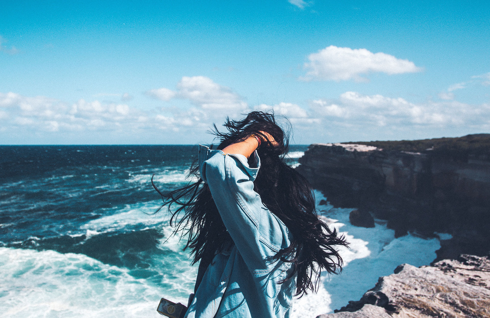 Girl on a rocky cliff by the ocean, with the wind in her hair