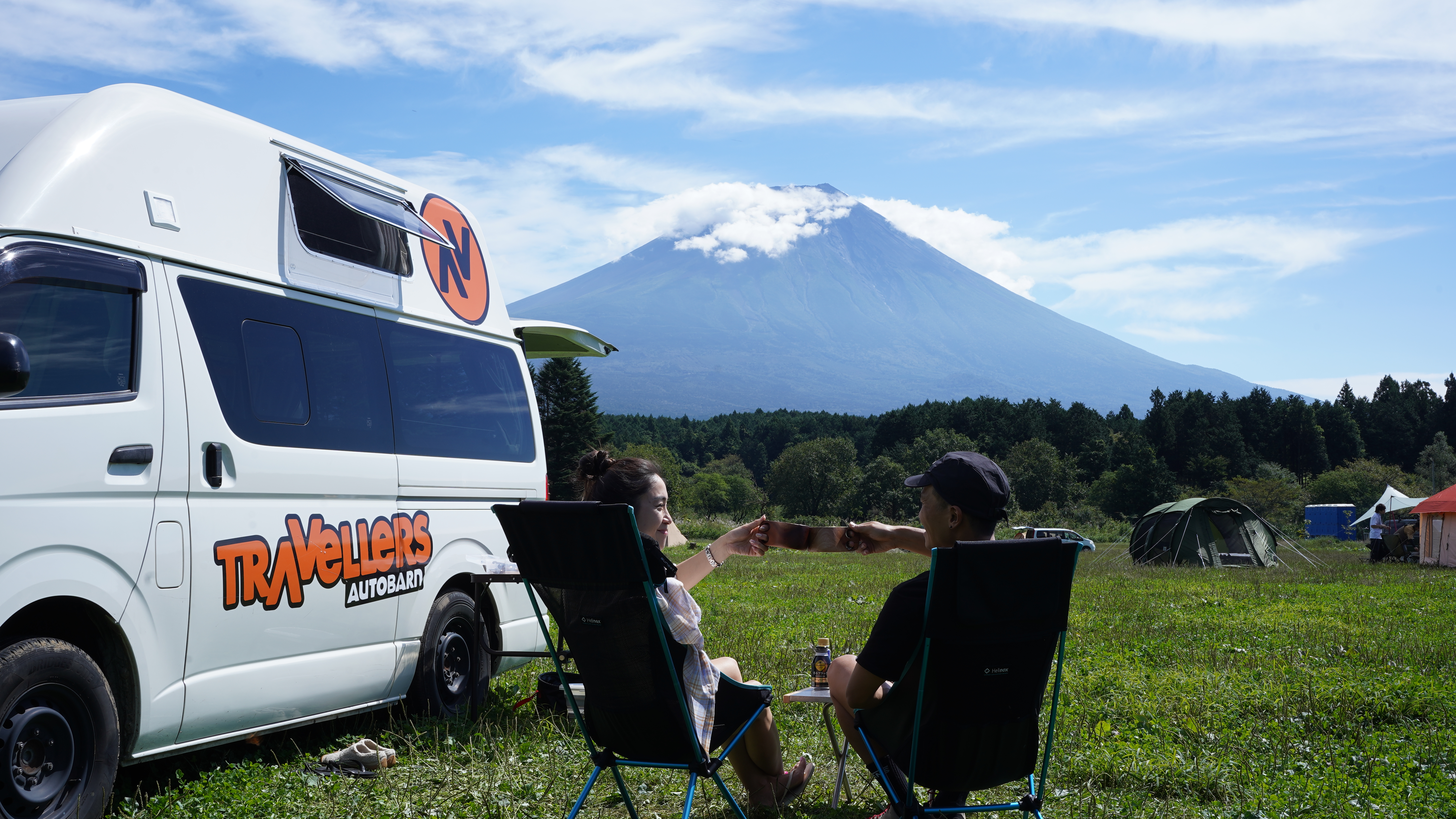 Campervan on a campsite in Japan, with a view of a volcano and other vans and tents in the background on the grassy field