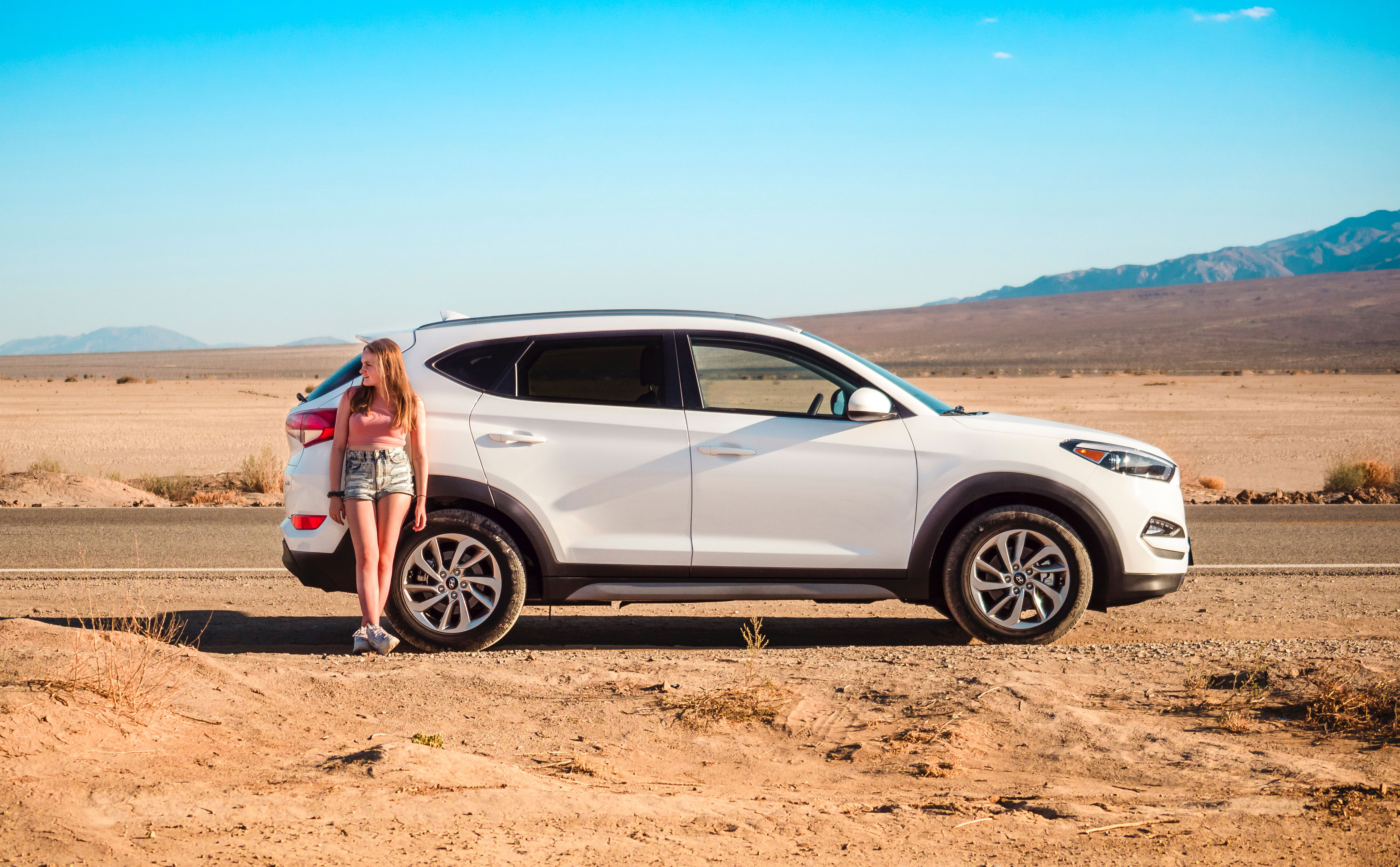 A young girl leaning against her rental car in Death Valley in California, USA