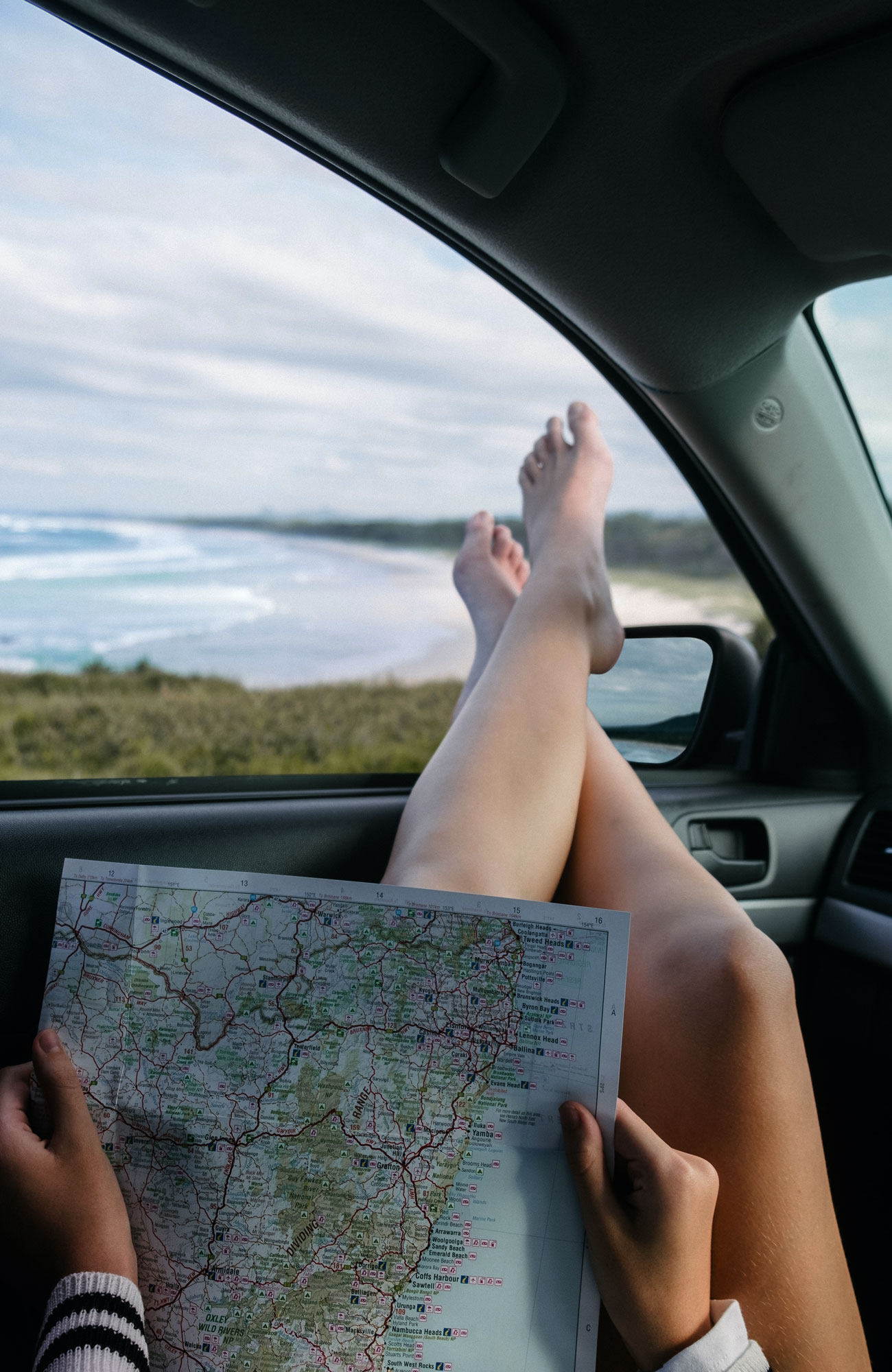 Solo Travel Beginners Guide - Women with map sticking legs out of a car window - Blog - KILROY