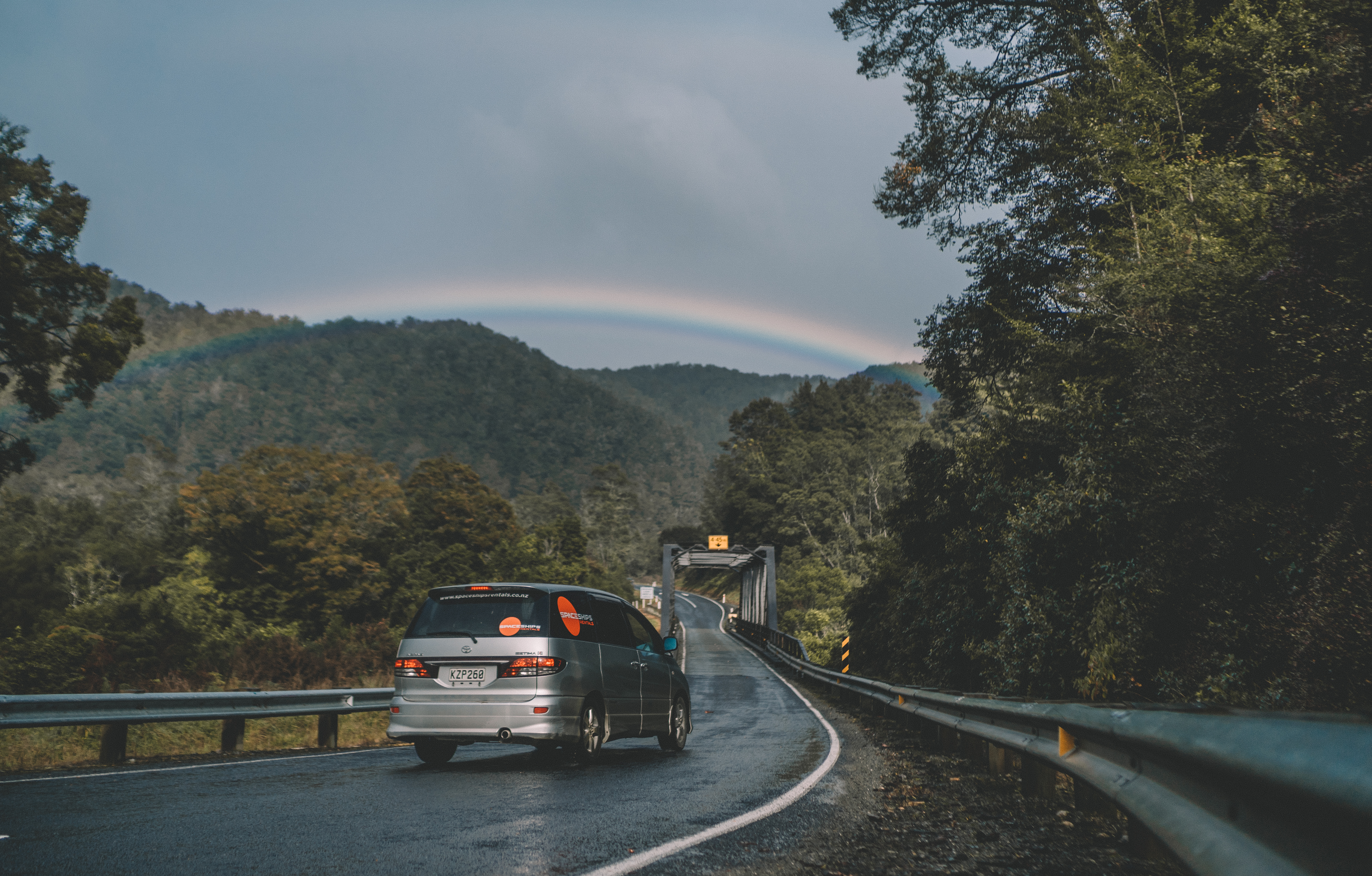 Grey Spaceships Campervan driving on a wet road through a green landscape in New Zealand.