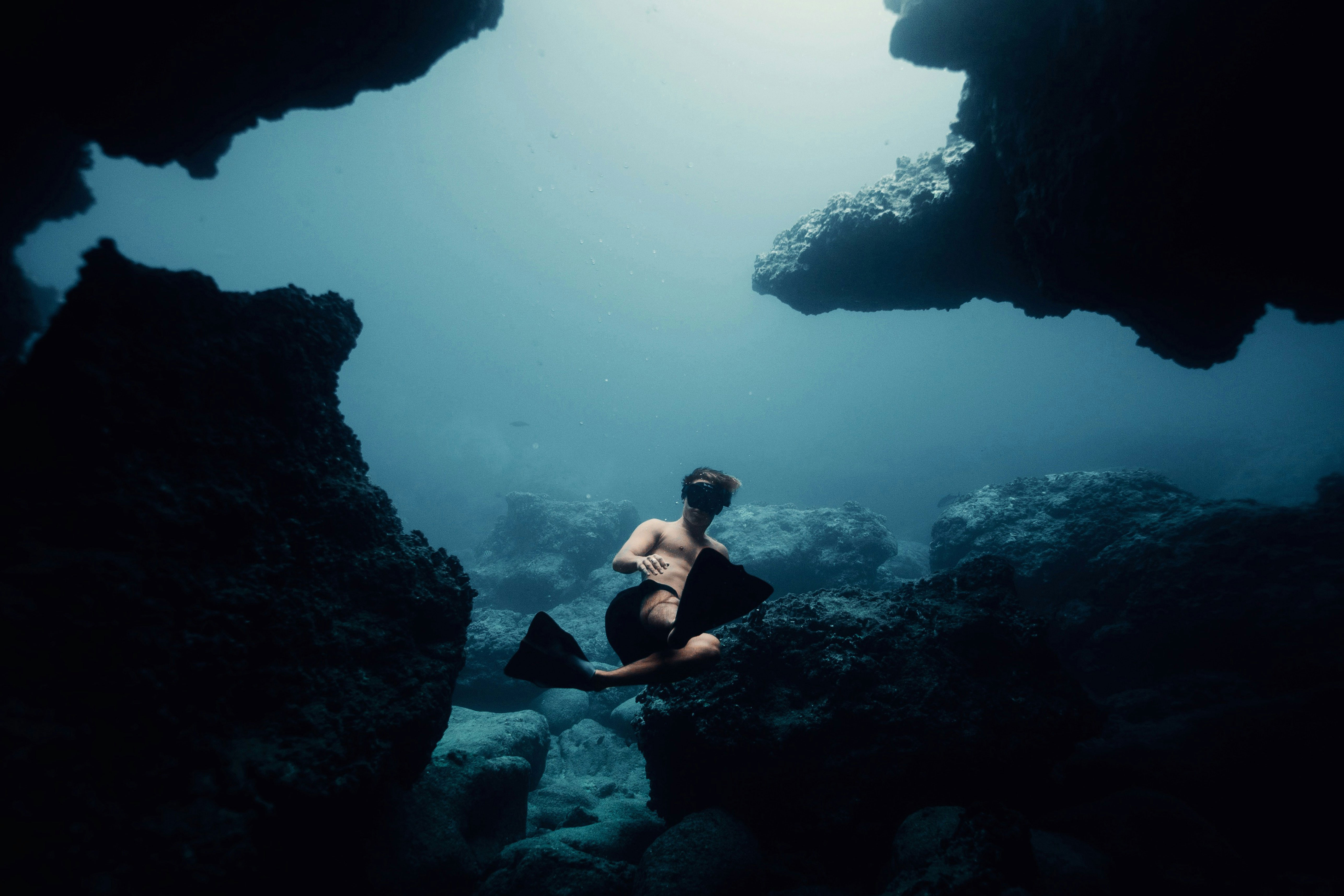 Freediver In The Ocean With A Lot Of Big Rocks Surrounding Him