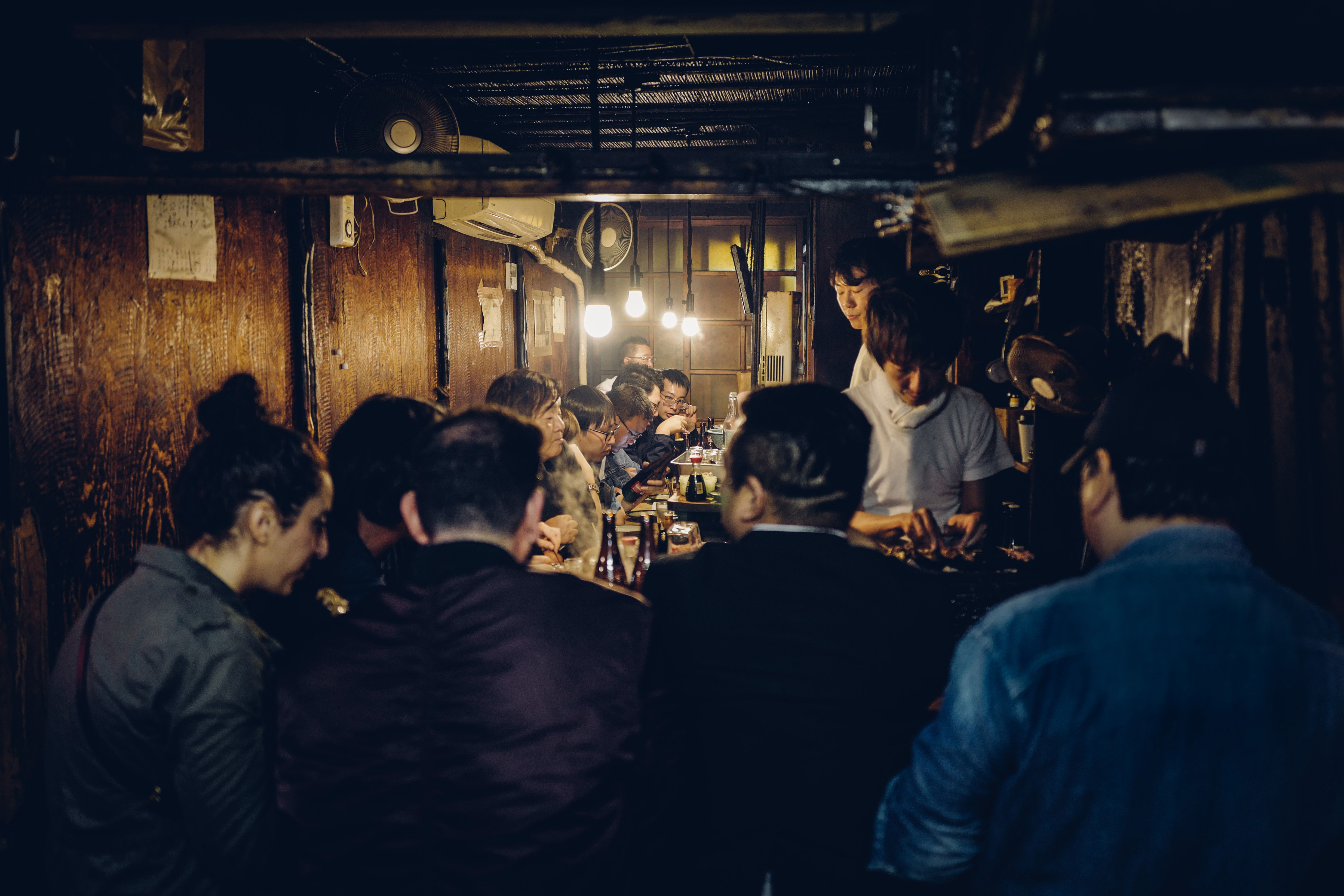 Group of people sitting around the bar in a pretty packed Izakaya somewhere in Japan
