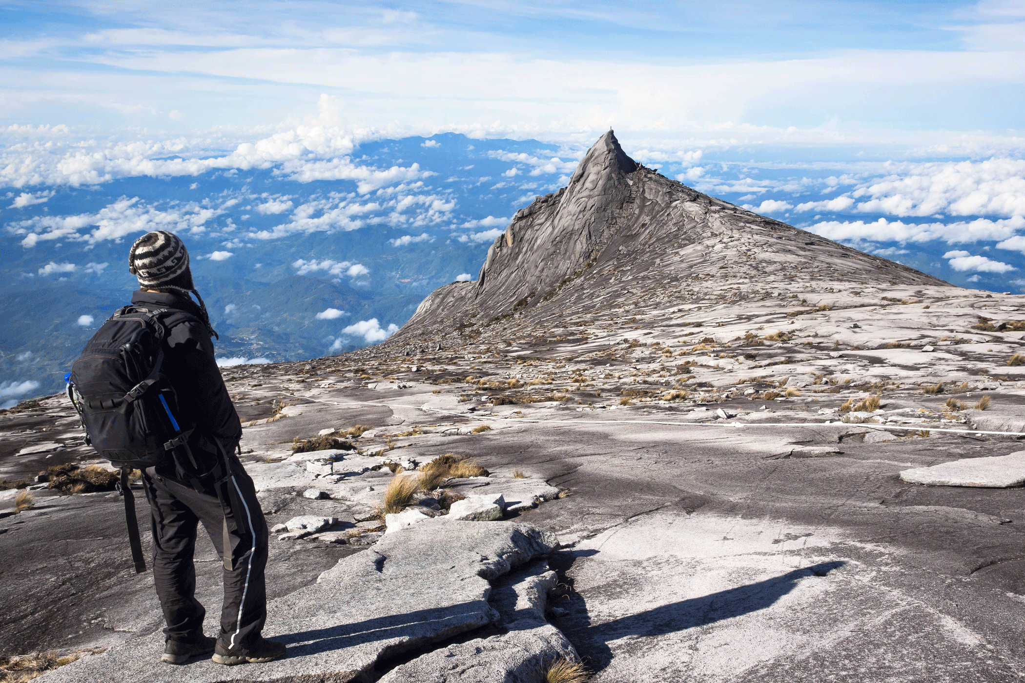 Man with a backpack dressed in black, standing on Mount Kinabalu on Borneo