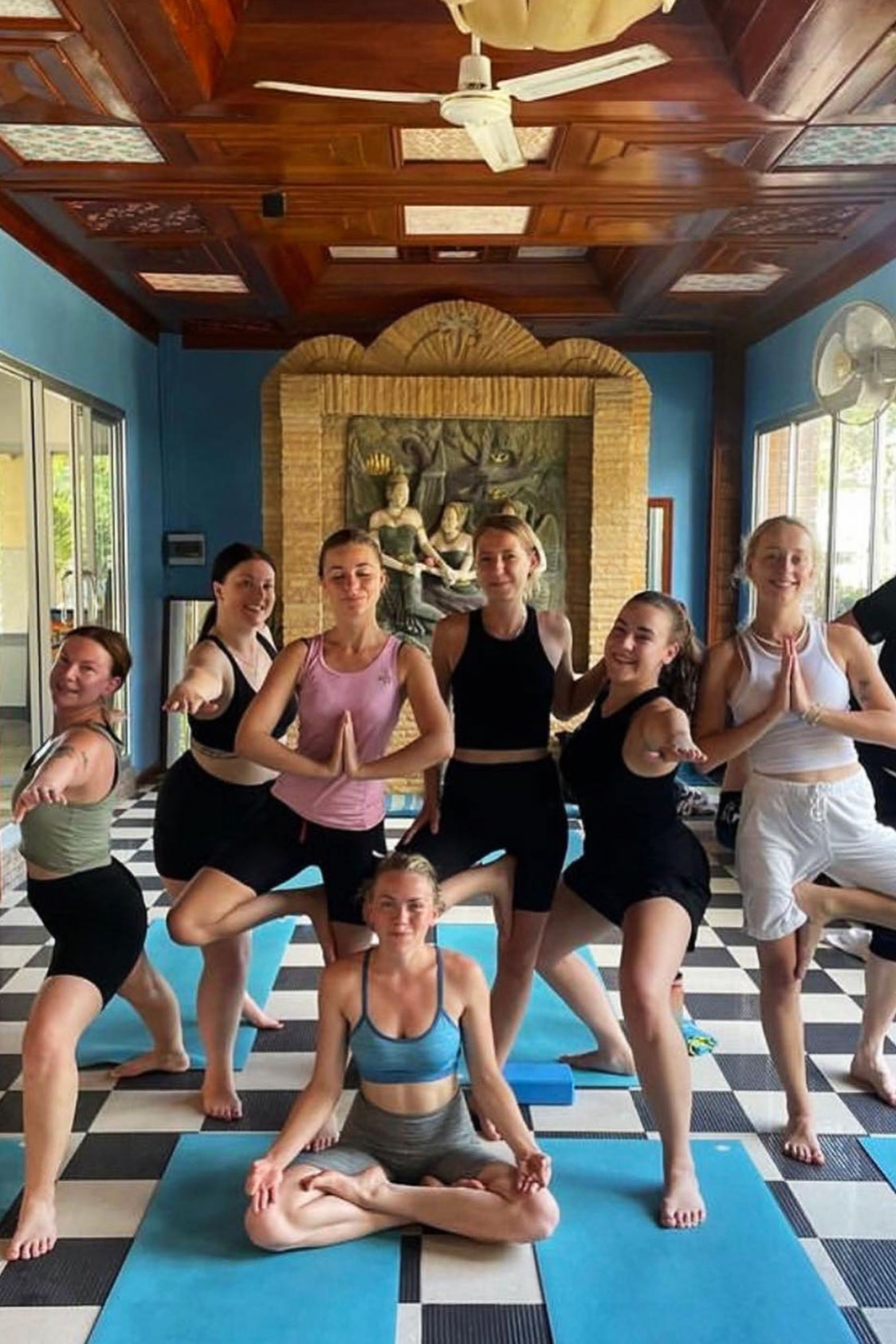 Freja and six other girls, standing and sitting on blue mats in a yoga retreat in Thailand