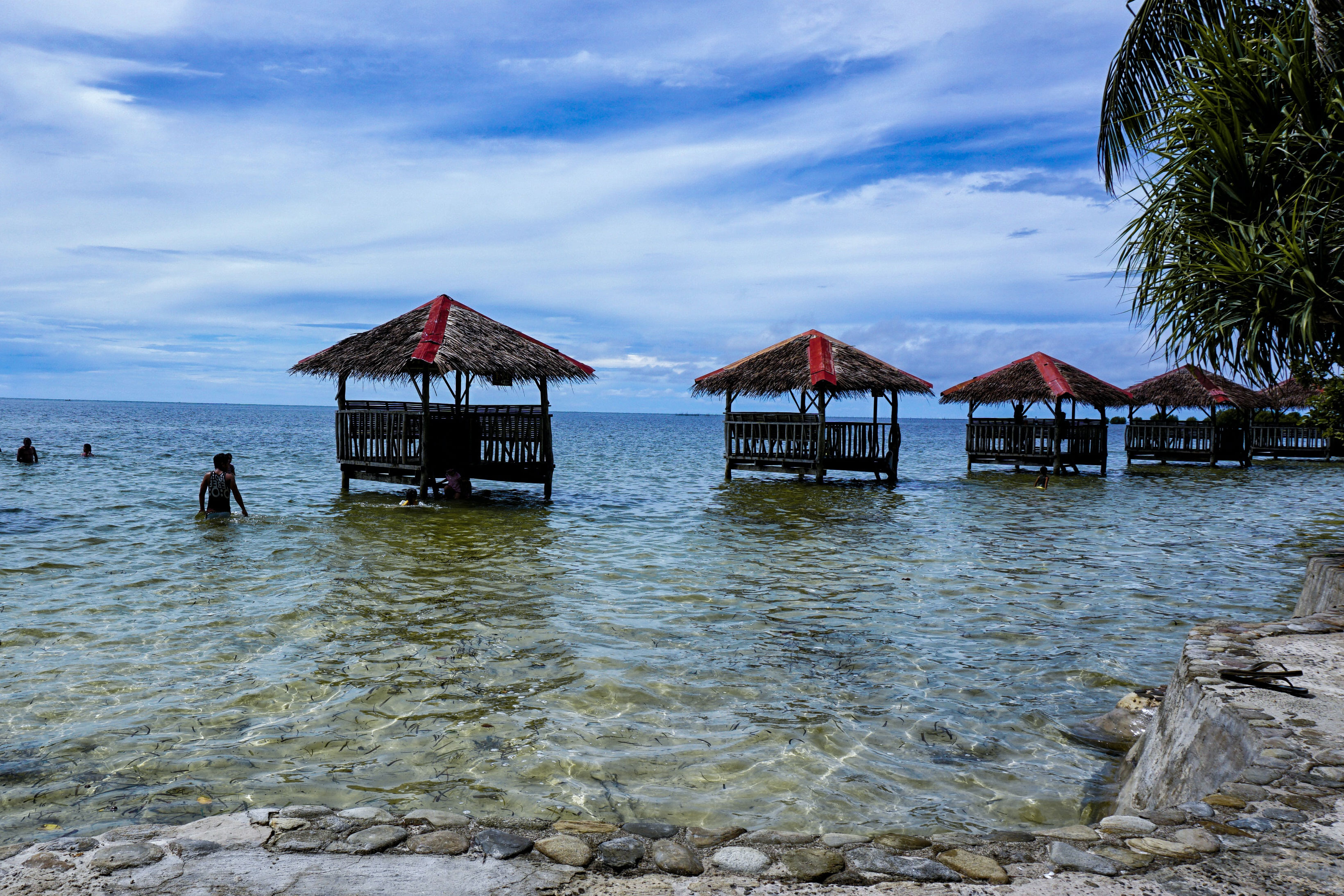 People swimming near huts out in the clear waters of Palawan in the Philippines